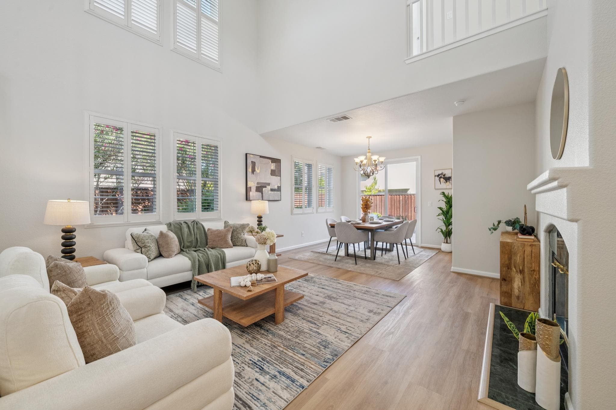 Bright double-height living room with fireplace, tall windows, open staircase, and dining area beyond
