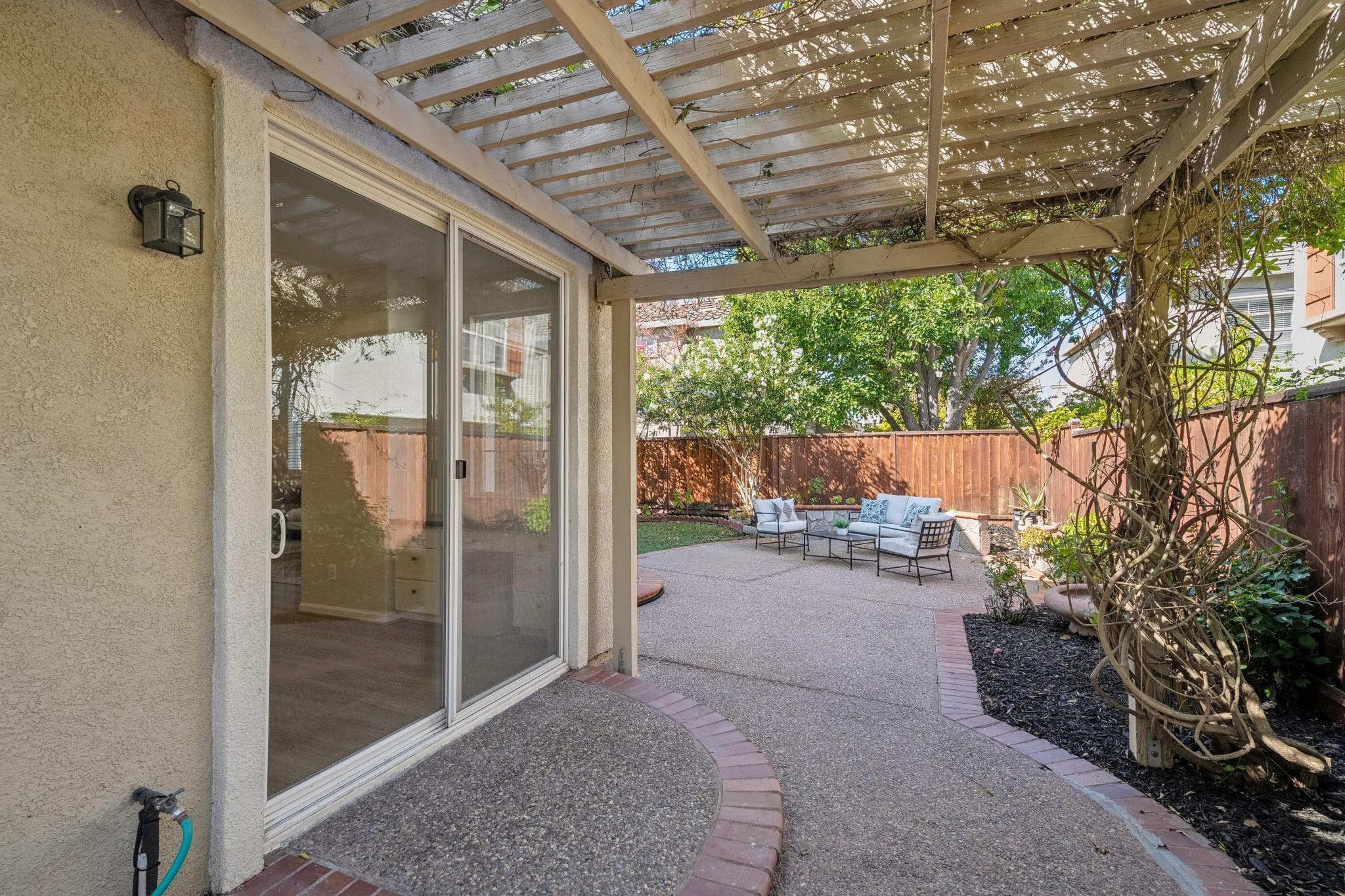 Vine-covered pergola framing the patio and sliding doors, with seating beyond